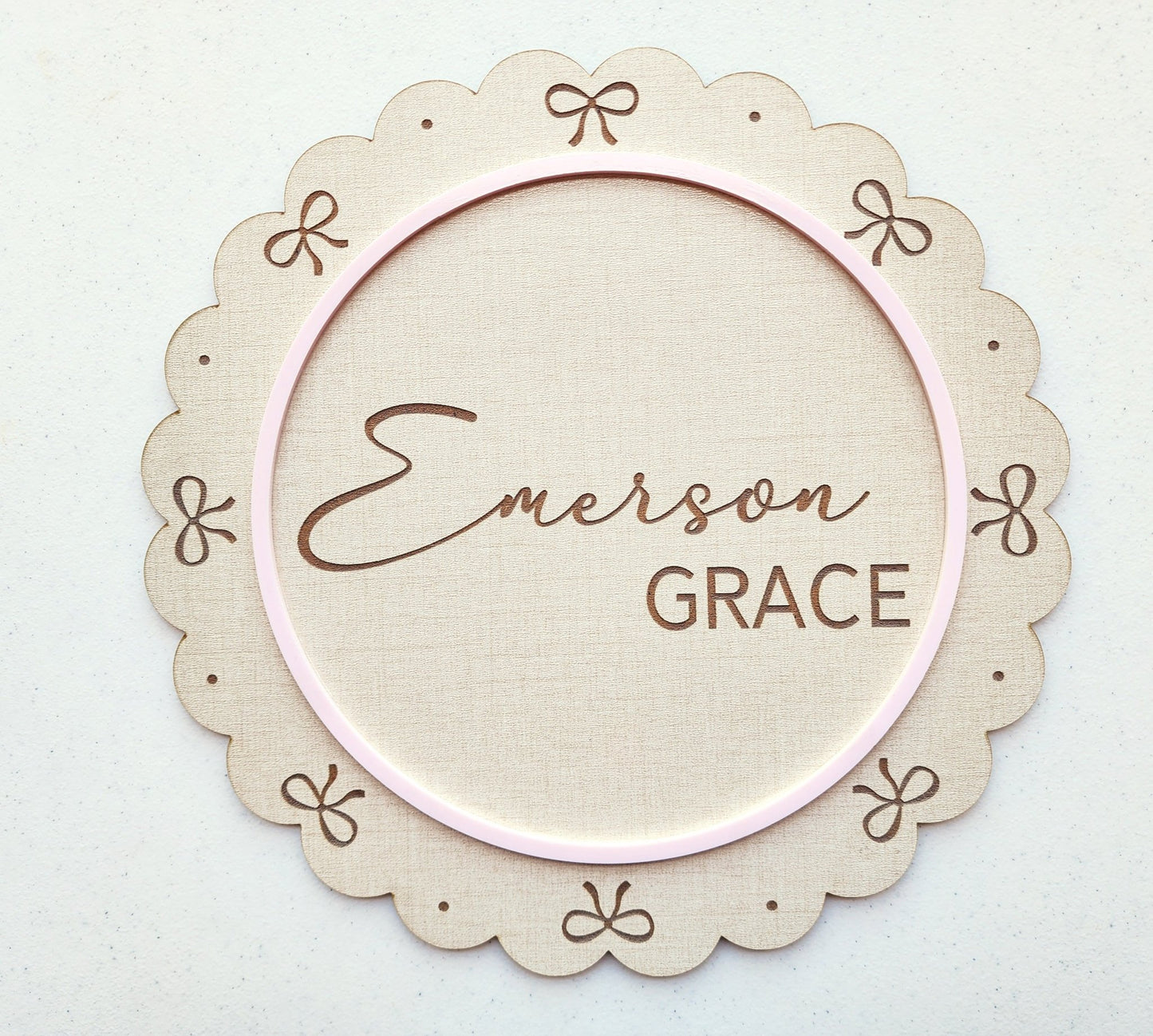 The Mirabilia Boutique Personalized Baby Name Shelf Sign features scalloped edges, delicate bows, custom name in script and bold text, and a thin pink border—a charming beige wooden nursery decor or newborn gift.