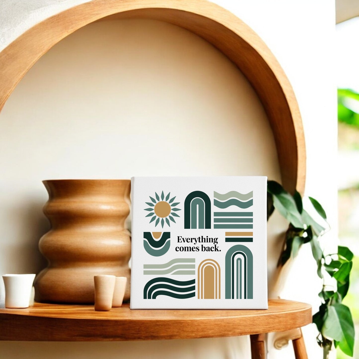 The Everything Comes Back Canvas by Mirabilia Boutique features earth-tone abstract shapes, a sun, and an uplifting quote—displayed on a shelf with vases and a trailing plant, it’s the perfect modern wall decor accent.