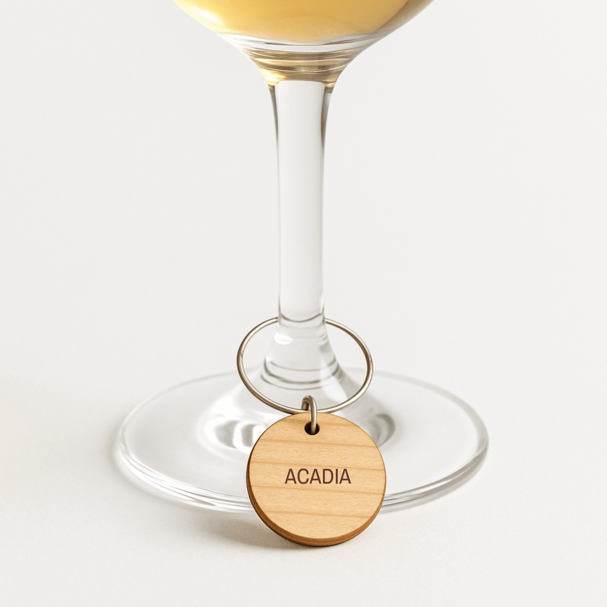 A wine glass features a wooden "ACADIA" charm on a metal ring from the Favorite National Parks Wine Charms by Mirabilia Boutique, shown against a plain white background.