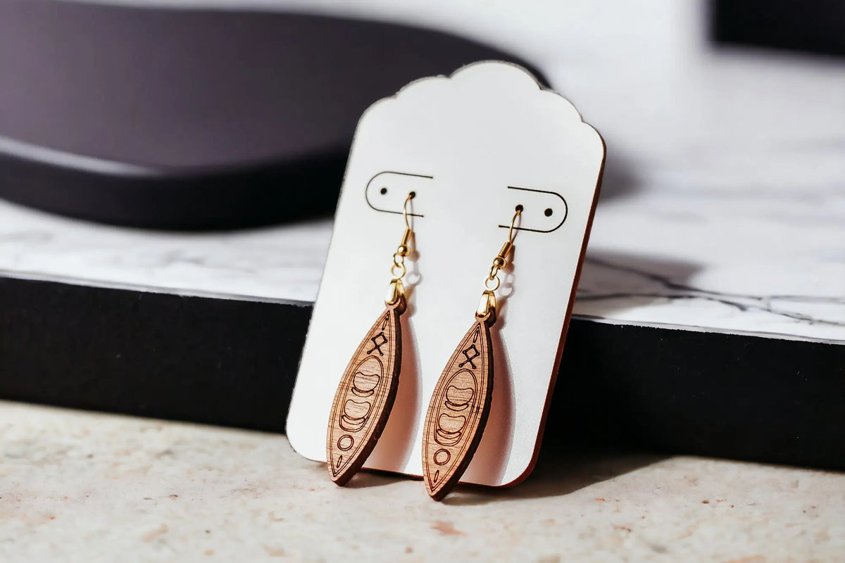 Kayak Earrings by Mirabilia Boutique—lightweight, laser-cut wooden dangle earrings with engraved designs on gold hooks, perfect for outdoor lovers, river girls, and paddlers. An ideal canoe gift, displayed on a white card with a marble-black background.