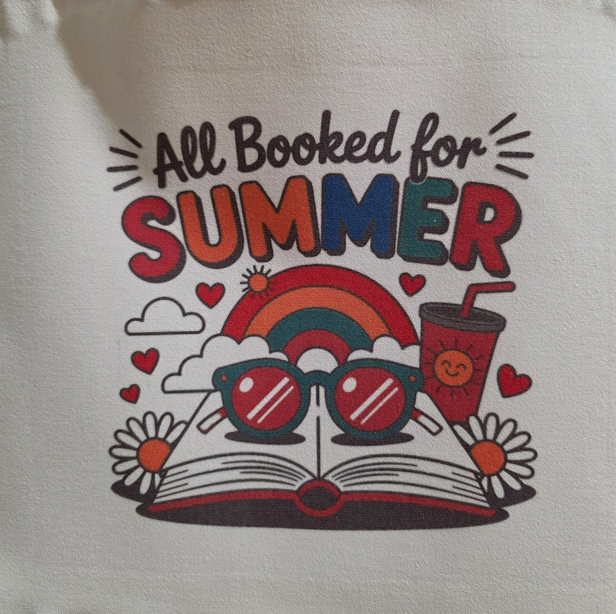 Featuring a retro design with "All Booked for SUMMER," an open book, sunglasses, rainbow, daisies, hearts, and a smiling drink cup on a light background, the Retro All Booked for Summer Tote Bag by Mirabilia Boutique is perfect for summer days.