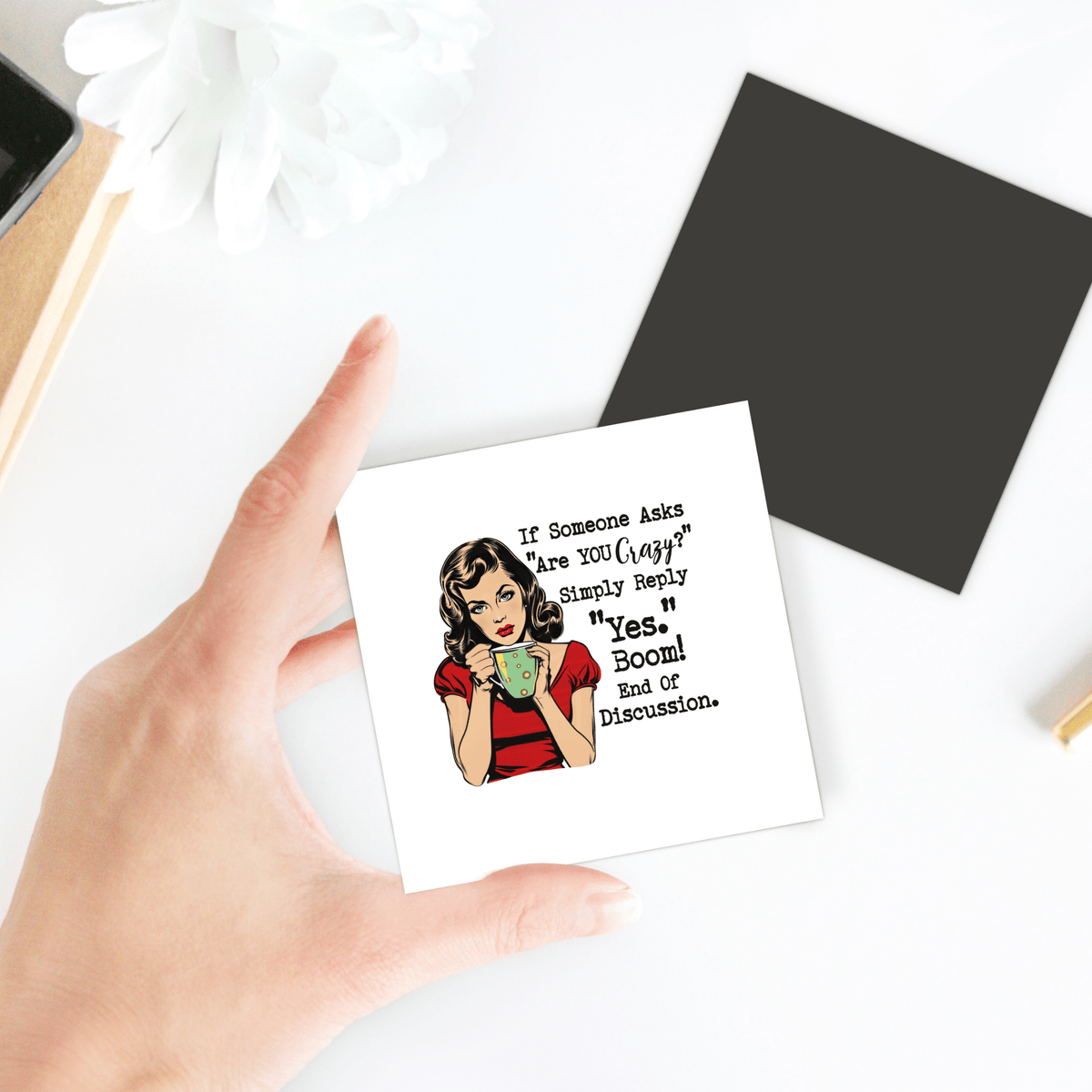 A hand holds the Funny “Are You Crazy?” 3x3 UV printed retro magnet by Mirabilia Boutique, featuring a woman with a cup and the quote: "If someone asks 'Are you okay?' Simply reply 'Yes. Boom! End of discussion." A sassy gift for friends or coworkers.