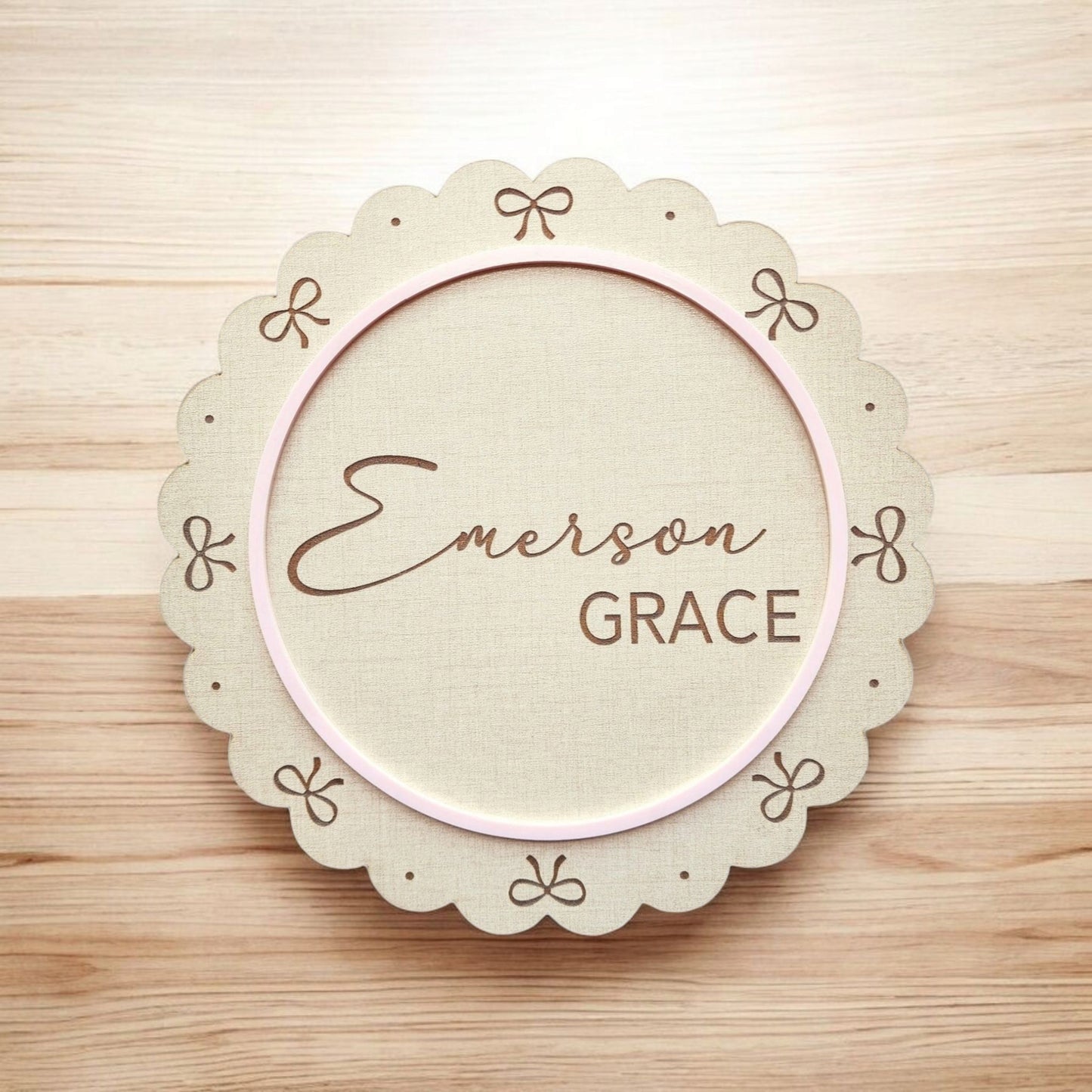 The Mirabilia Boutique Personalized Baby Name Shelf Sign features a scalloped wooden plaque with bow accents, a pink circle border, and the name "Emerson Grace" in script and block—perfect as custom nursery decor or a newborn gift.
