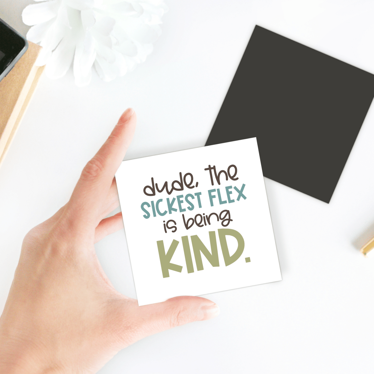 The Mirabilia Boutique Sickest Flex Is Being Kind Magnet shows a hand holding a card that reads, "dude, the SICKEST FLEX is being KIND," with a black square and white flower in the background—perfect for classroom décor or gifts.