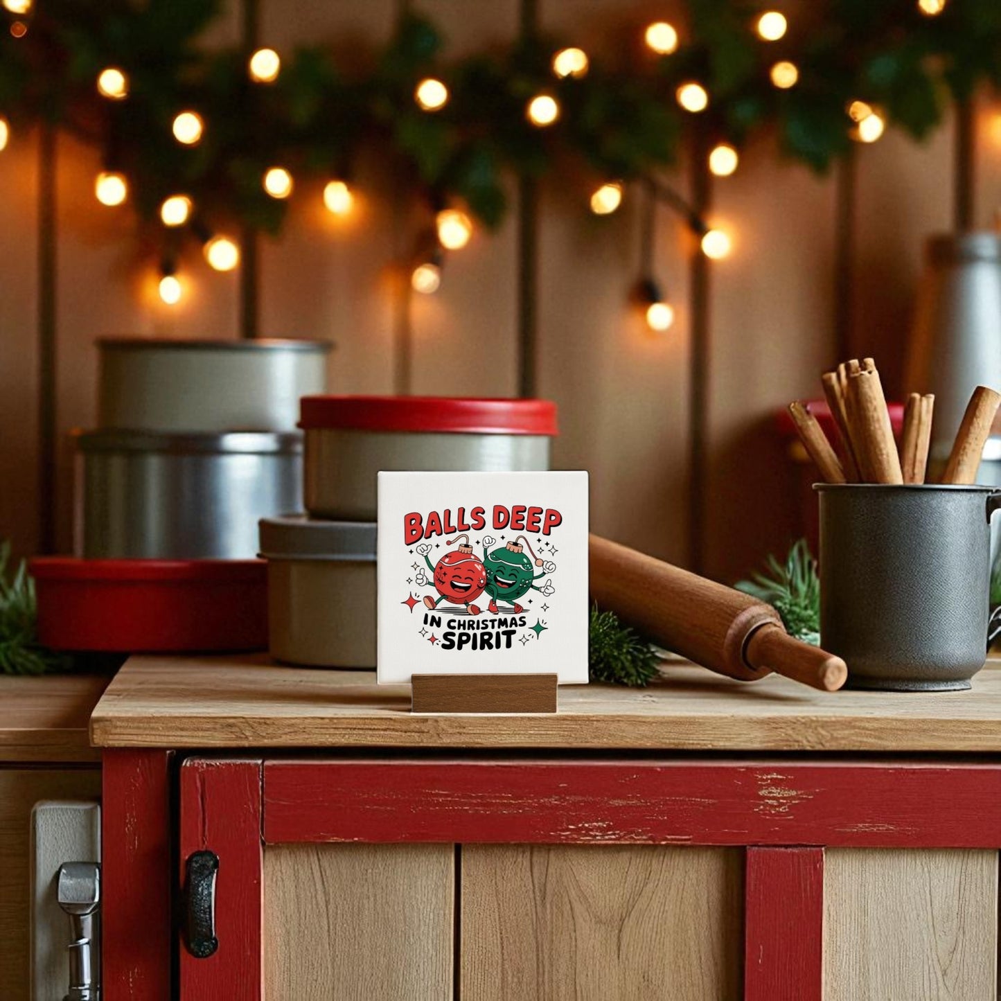 A festive kitchen features the "Balls Deep in Christmas Spirit" funny mini holiday sign by Mirabilia Boutique, with two smiling ornaments—perfect adult Christmas decor for your counter alongside tins and a mug of cinnamon sticks.