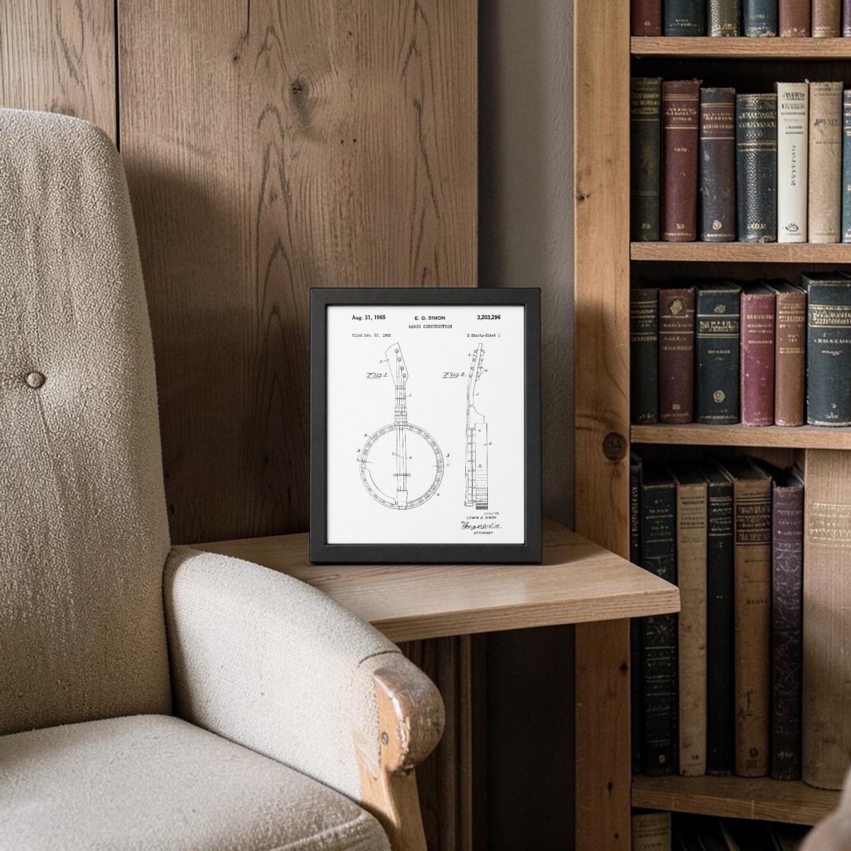 The Banjo Patent Print 8x10 Wall Art by Mirabilia Boutique is displayed on a wooden side table beside a beige armchair, with bookshelves and wooden cabinets behind, adding vintage musical charm to a cozy reading nook.