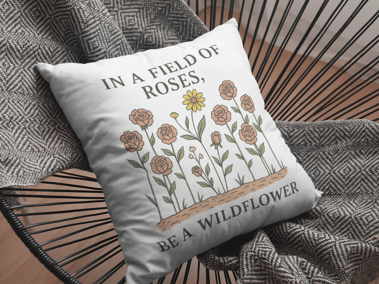 Add a nature-inspired touch to your boho decor with the Be a Wildflower Throw Pillow by Mirabilia Boutique, featuring illustrated roses, a yellow wildflower, and the quote "In a field of roses, be a wildflower.