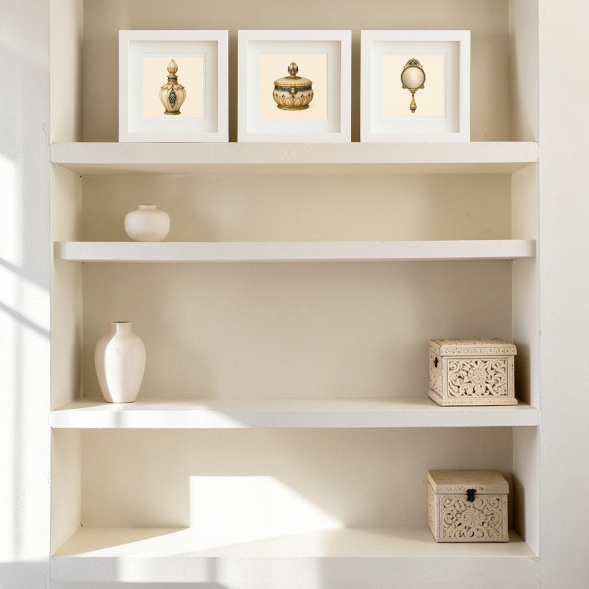 White built-in shelves showcase three framed canvas artworks on the top shelf, two white vases to the left, and two ornate Beauty Rituals of the Nile Relics by Mirabilia Boutique displayed on the lower right shelves, all illuminated by natural sunlight.