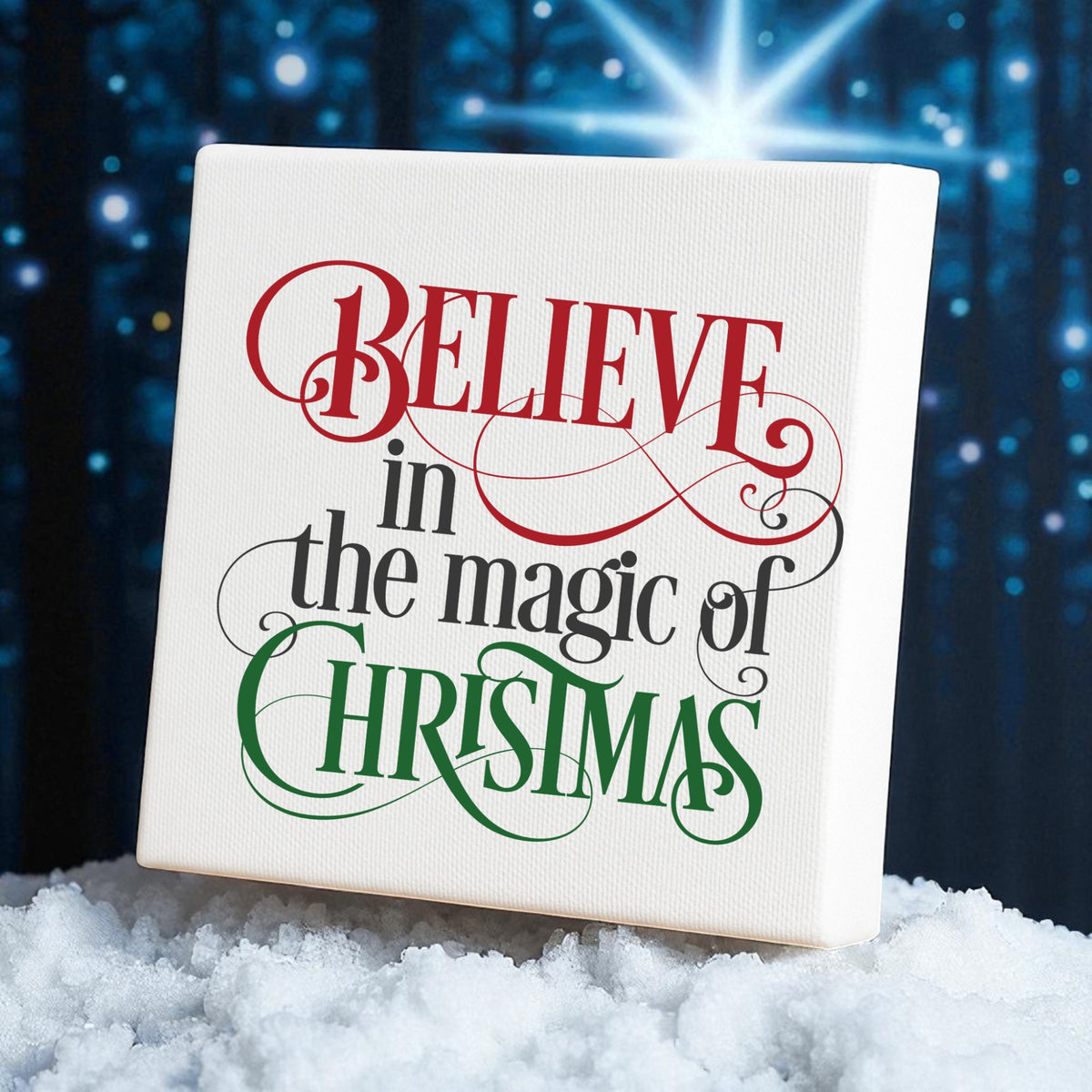 The "Believe in the Magic of Christmas" Wall Art by Mirabilia Boutique features festive lettering, resting on faux snow with twinkling lights and a glowing star, set against a blue background—perfect holiday decor.