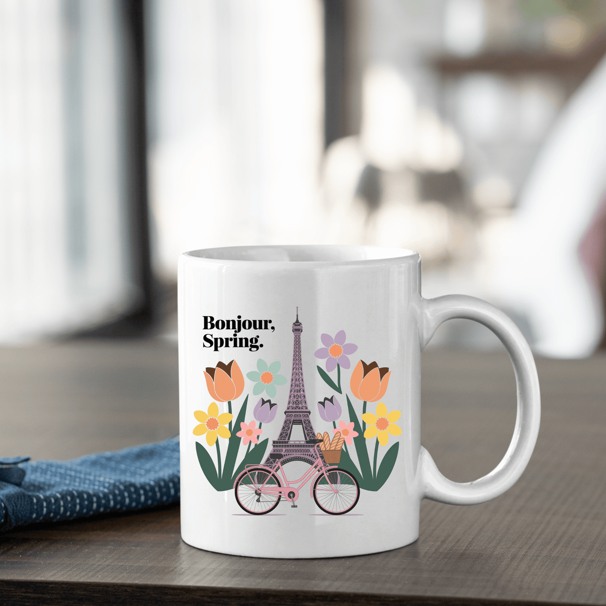 The Mirabilia Boutique "Bonjour Spring Paris Mug – Eiffel Tower & Florals" features an illustration of the Eiffel Tower, colorful flowers, and a pink bicycle with "Bonjour, Spring." in black text.