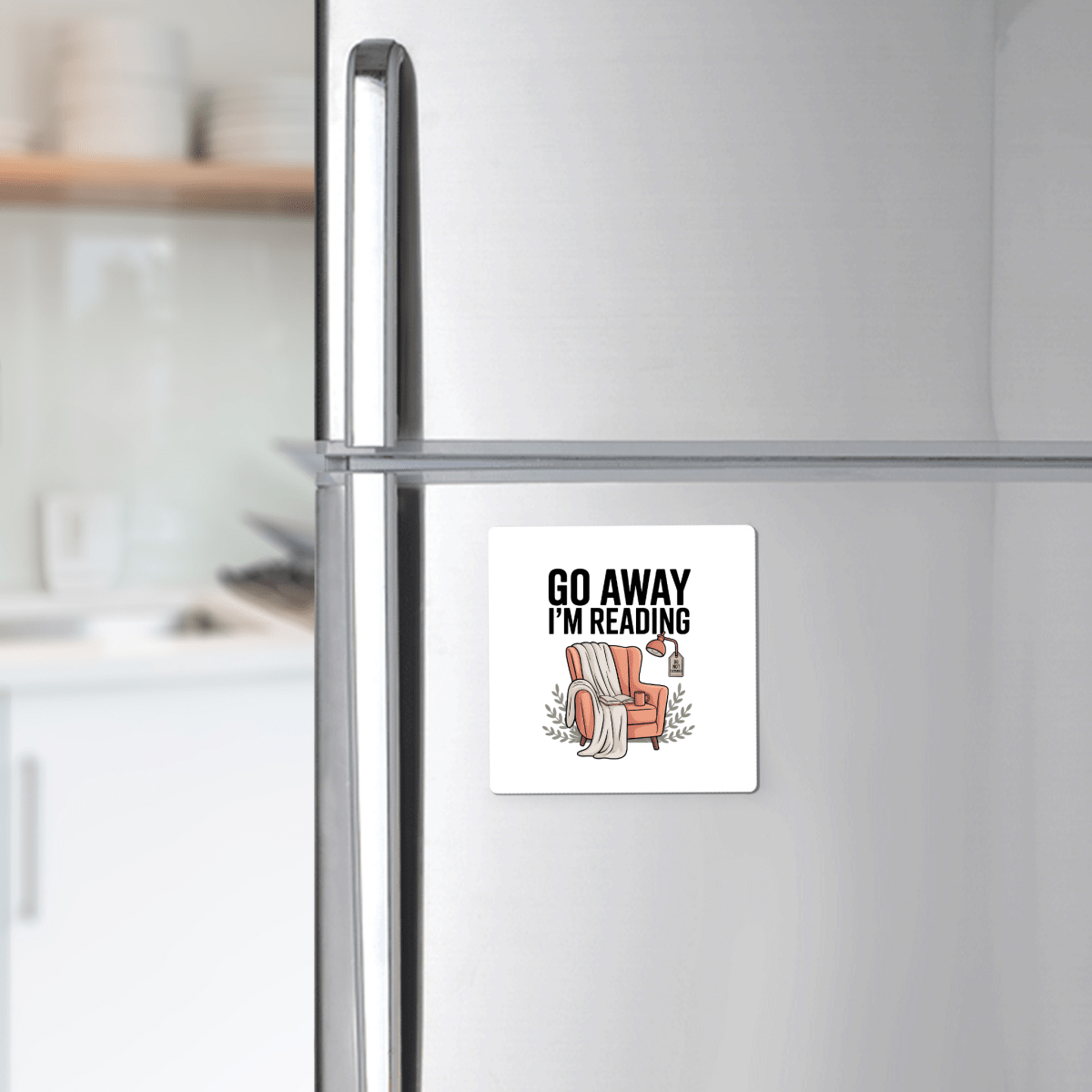 The Go Away I'm Reading Magnet by Mirabilia Boutique features "GO AWAY I'M READING" above a cozy armchair, book, and coffee. This funny book lover gift makes perfect decor for any reader’s fridge.