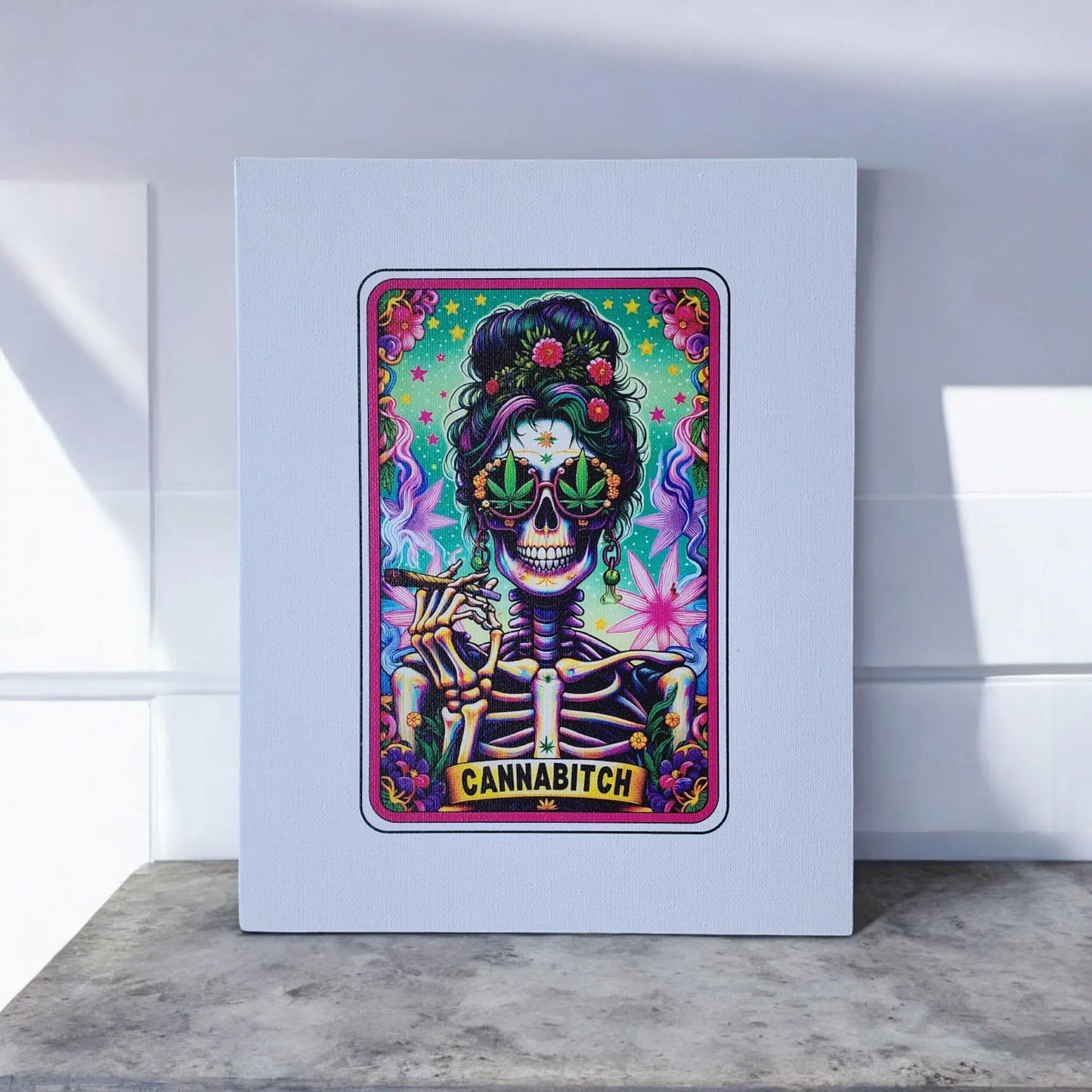 A vibrant and intricate artwork featuring a skeleton wearing sunglasses, adorned with flowers and holding a joint, with the word "CANNABITCH" displayed at the bottom. The Mirabilia Boutique's Cannabitch 8x10 Canvas Sign is mounted on a white canvas and elegantly propped up on a marble surface against a white wall with shadows.