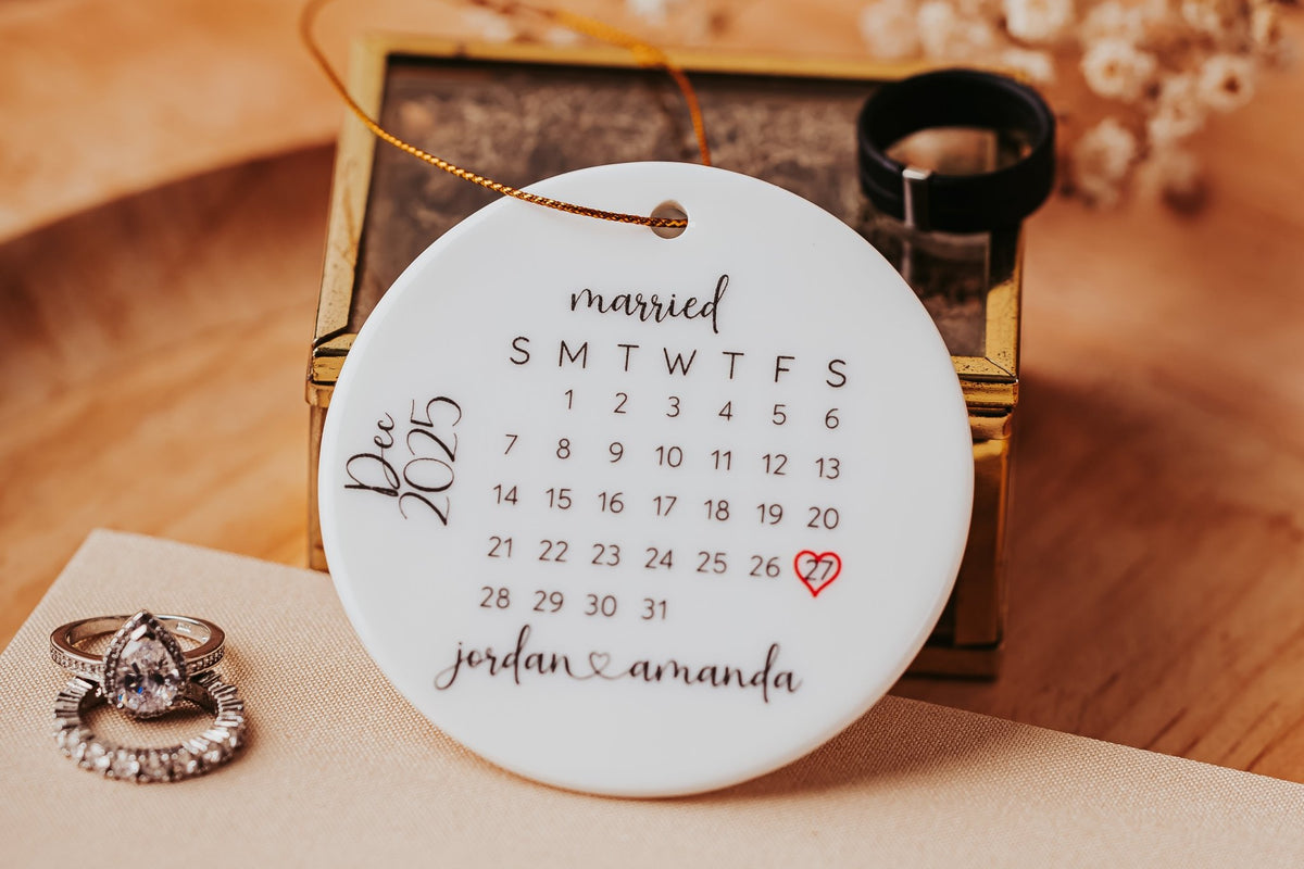 The Mirabilia Boutique Personalized Wedding Date Ornament is a custom ceramic calendar keepsake featuring "married" at the top, "jordan & amanda" below, and a red heart on Dec 20th—an ideal gift for newlyweds.