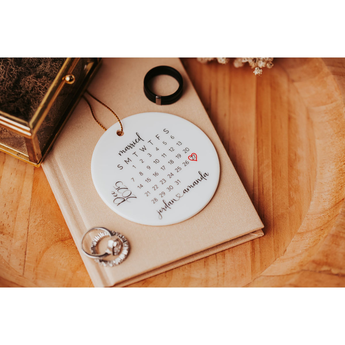 The Personalized Wedding Date Ornament – Custom Ceramic Calendar Keepsake by Mirabilia Boutique features a calendar with a red heart marking your special date, "John & Amanda" beside rings, and is a perfect bridal shower or newlywed gift.
