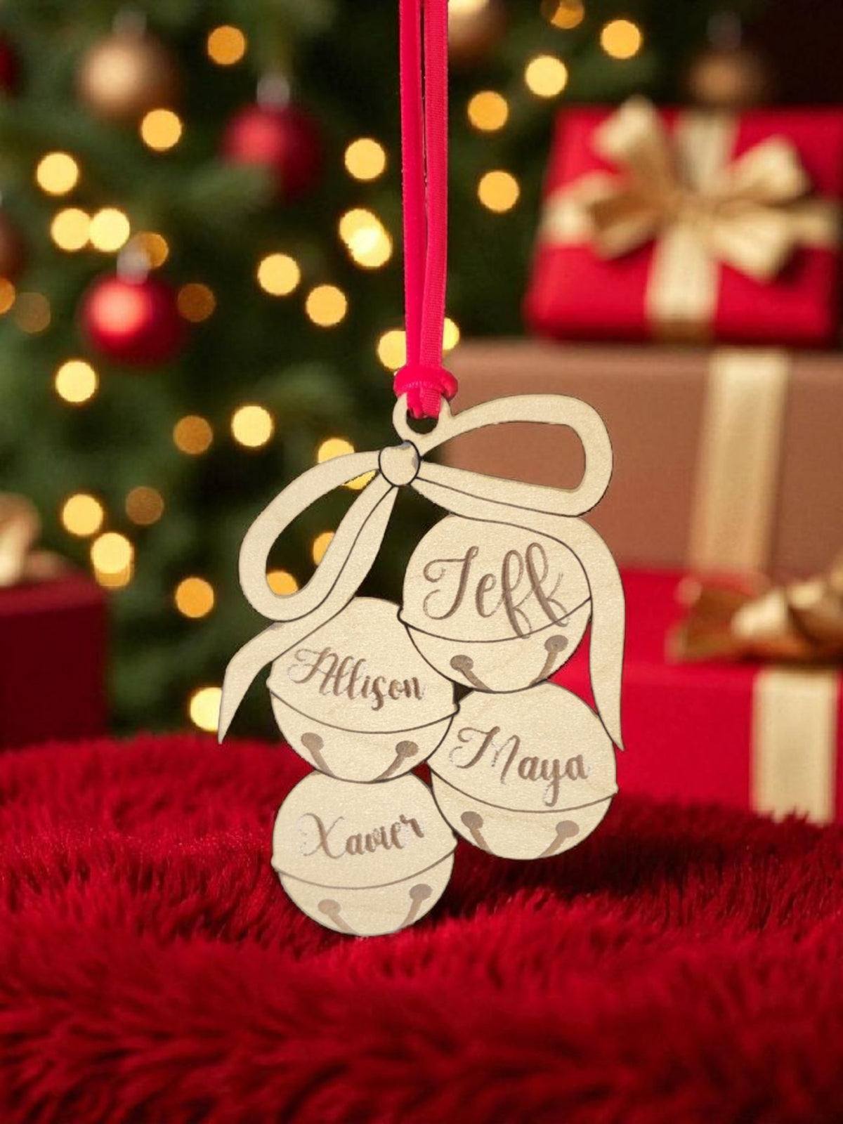 The Mirabilia Boutique Custom Family Christmas Ornament is a laser-cut wooden jingle bell featuring four names—Jeff, Allison, Xaver, and Inaya—on a red ribbon, perfect for adding a festive touch to your holiday tree.