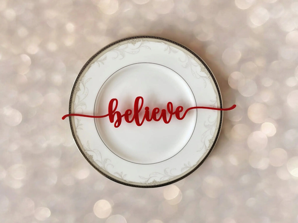 The Mirabilia Boutique Red Acrylic Christmas Plate Words, part of an 8-piece holiday table decor set, features "believe" in red cursive across a white plate with a decorative border, perfect for your festive table setting.
