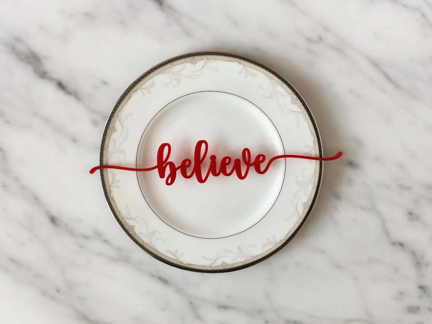 The Mirabilia Boutique Red Acrylic Christmas Plate Words – 8 Piece Holiday Table Decor Set features festive red script cutouts that add modern holiday charm to your table, displayed here on a decorative white plate with a silver rim.