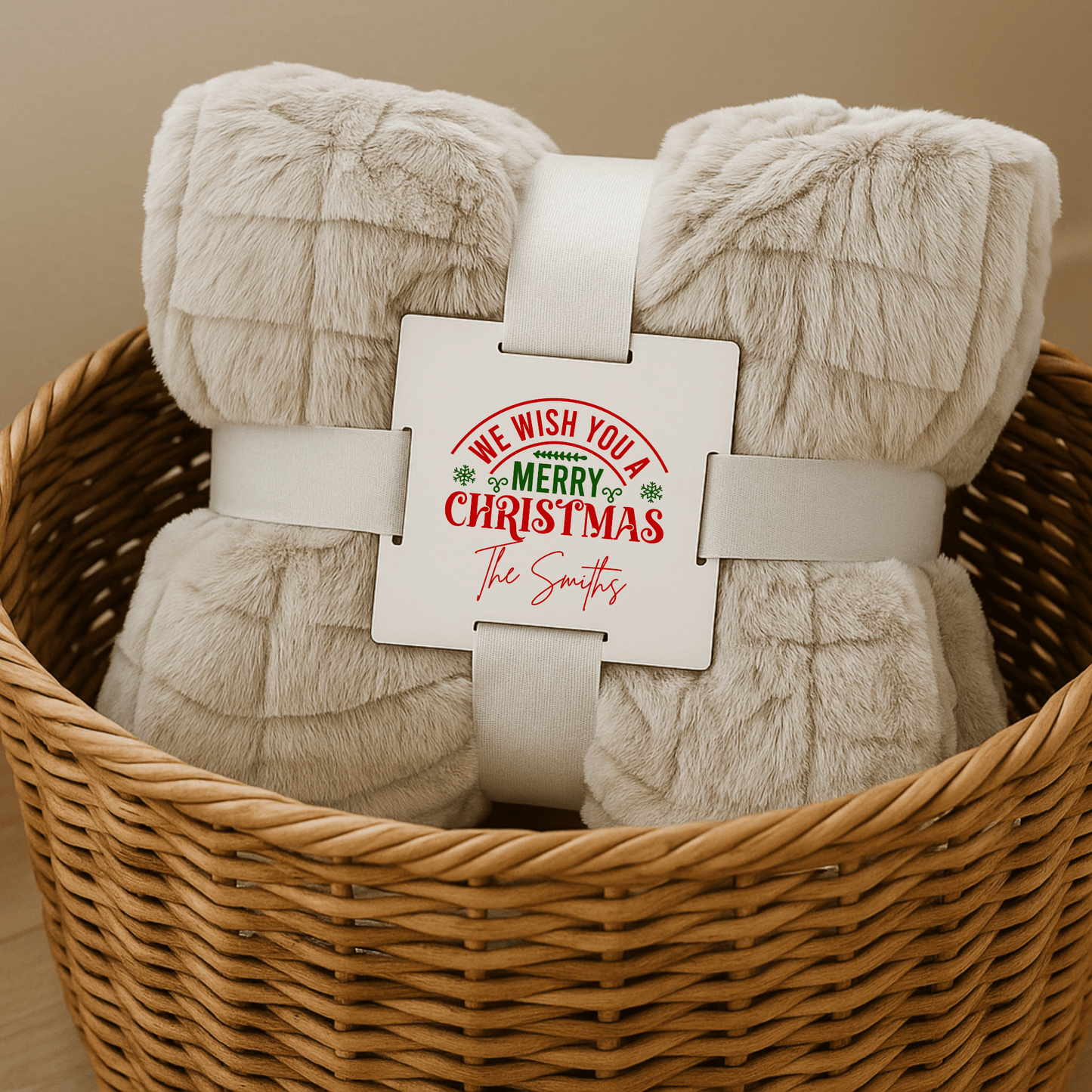 A beige Custom Christmas Throw Blanket from Mirabilia Boutique, rolled with a white band in a wicker basket, features "We wish you a Merry Christmas" and your family name—making it the perfect cozy holiday gift for home.
