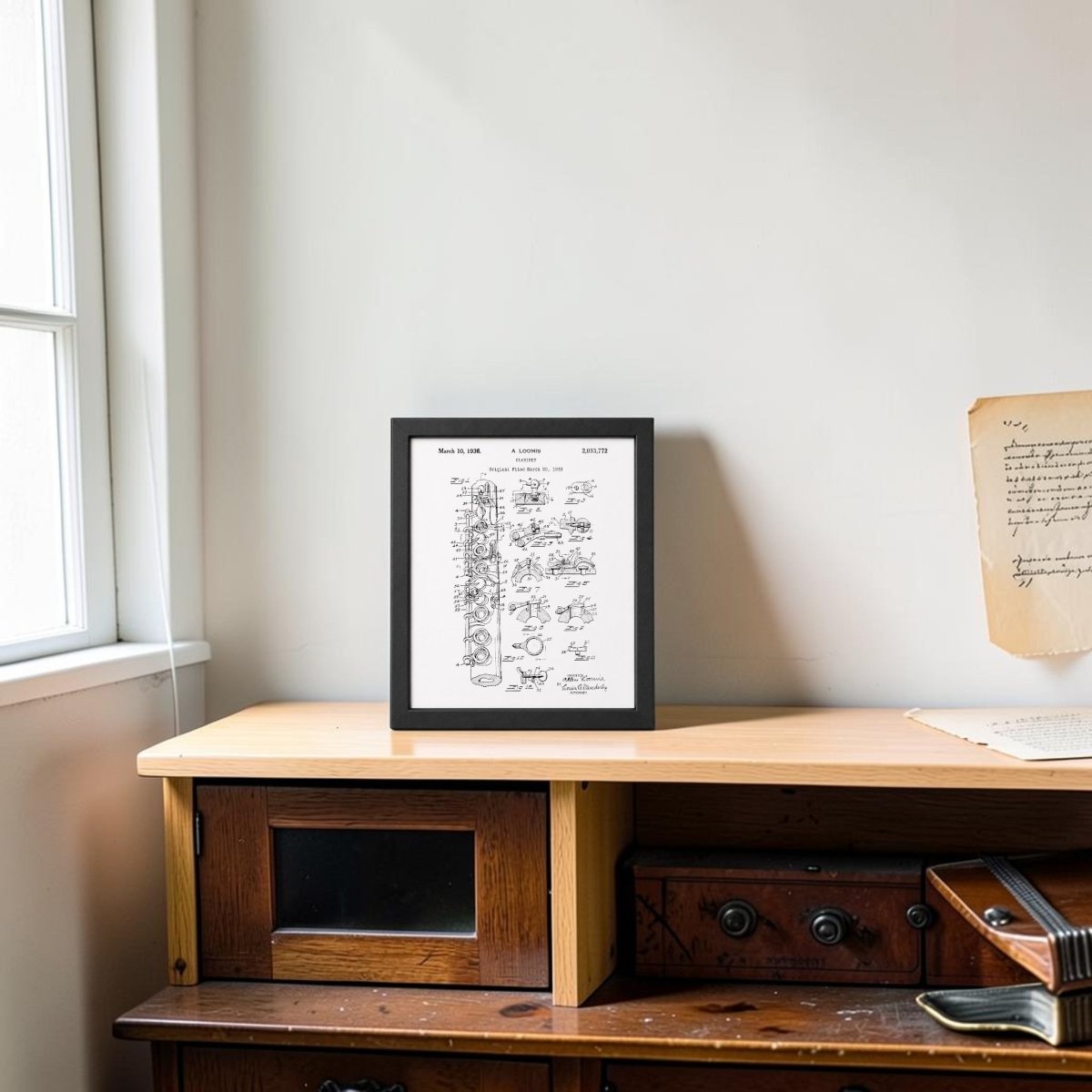 The Clarinet Patent Print on Metal Wall Art by Mirabilia Boutique sits on a light wooden cabinet by a window, with a handwritten letter pinned above—an elegant touch for music room decor.
