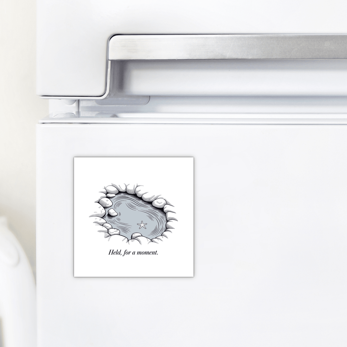The "Held, for a Moment – Coastal Reflection Magnet" by Mirabilia Boutique adorns your fridge with a serene pond, rocks, starfish, and grass. The calming design features the phrase “Held for a moment”—a soothing ocean-inspired decor accent.