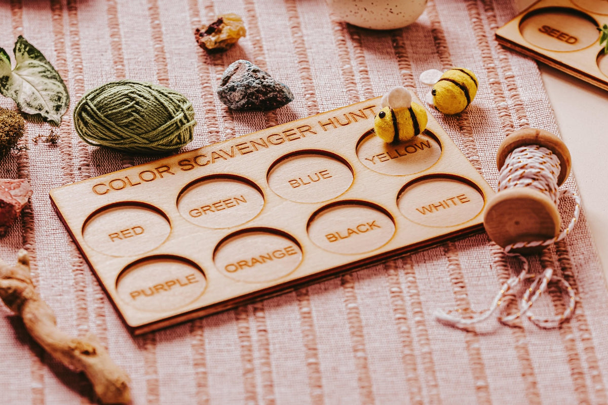The Mirabilia Boutique Wooden Color Scavenger Hunt Board is a laser-engraved, Montessori outdoor toy for kids—shown with nature items and toys on a pink striped fabric. It's a reusable, screen-free game for fun color-based learning activities.