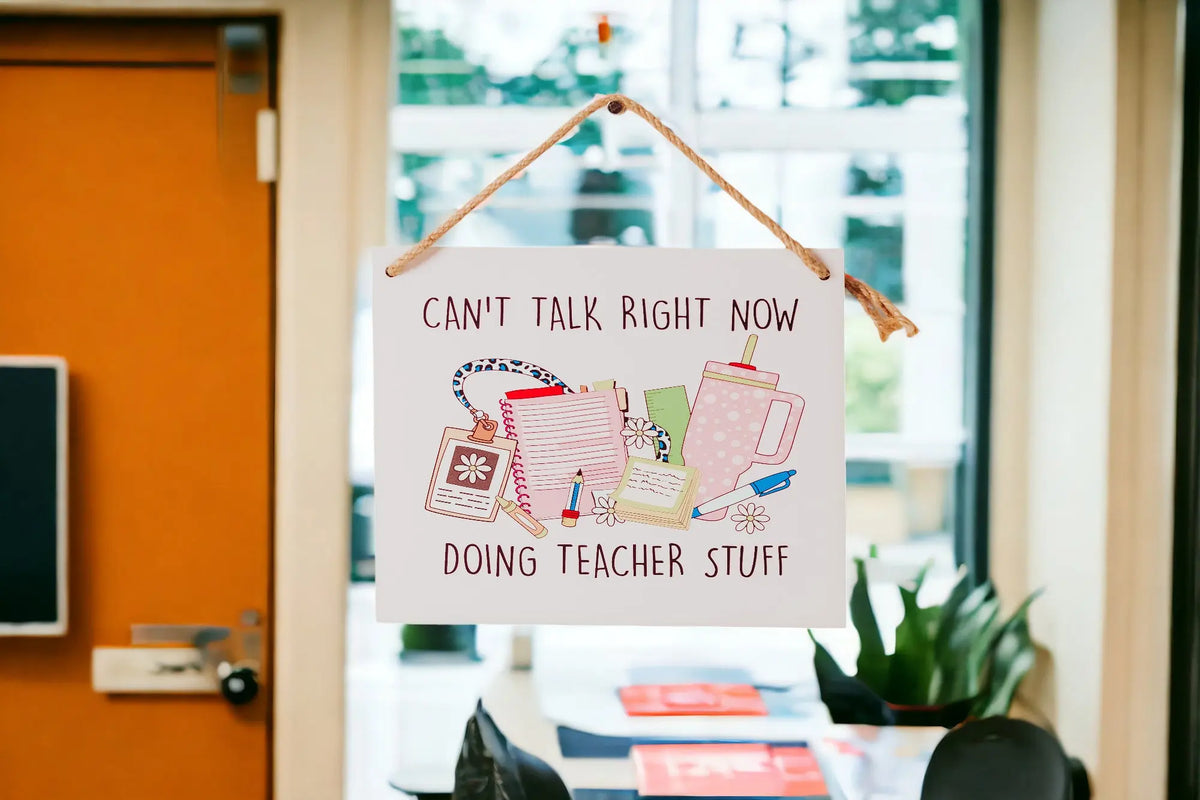 The Mirabilia Boutique Funny Teacher Door Sign reads "Can’t Talk Doing Teacher Stuff" and features notebooks, pens, a tumbler, and lanyard—making it a perfect classroom decor or back-to-school teacher gift. Classroom backdrop included.