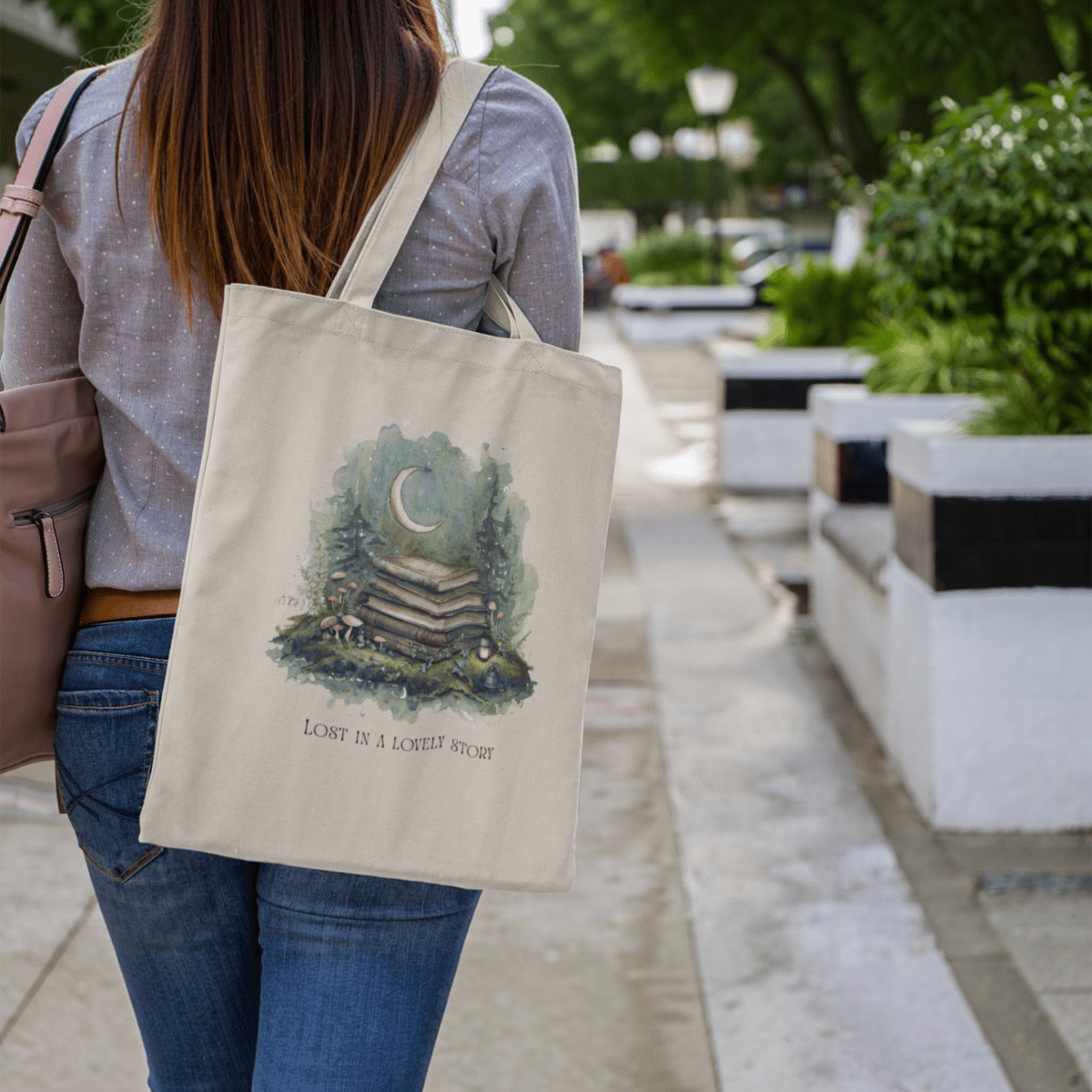 A woman walks on a sidewalk carrying the Lost in a Lovely Story Canvas Tote Bag from Mirabilia Boutique, featuring an illustration of books, a crescent moon, and the phrase "LOST IN A LOVELY STORY." This stylish literary tote makes the perfect gift for any book lover.