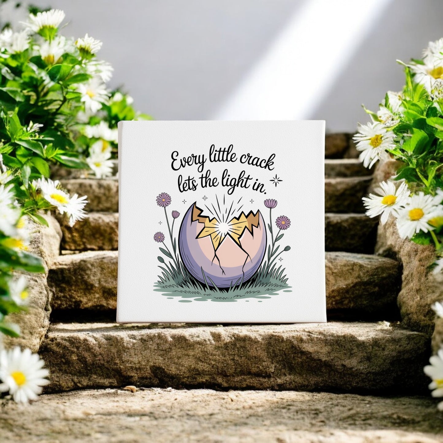 The Mirabilia Boutique "Every Little Crack Lets the Light In" canvas art features a cracked egg shining light on stone steps amid daisies, with the quote: “Every little crack lets the light in.” Inspiring decor for any space.