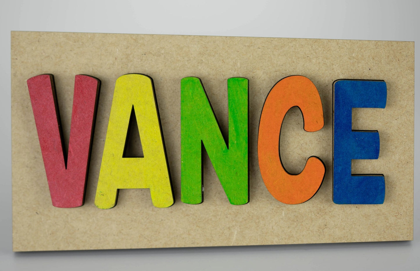 The Personalized Wooden Name Puzzle – Custom Rainbow Kids Sign by Mirabilia Boutique features handcrafted letters spelling "VANCE" in vibrant red, yellow, green, orange, and blue on a beige board for a charming custom gift.