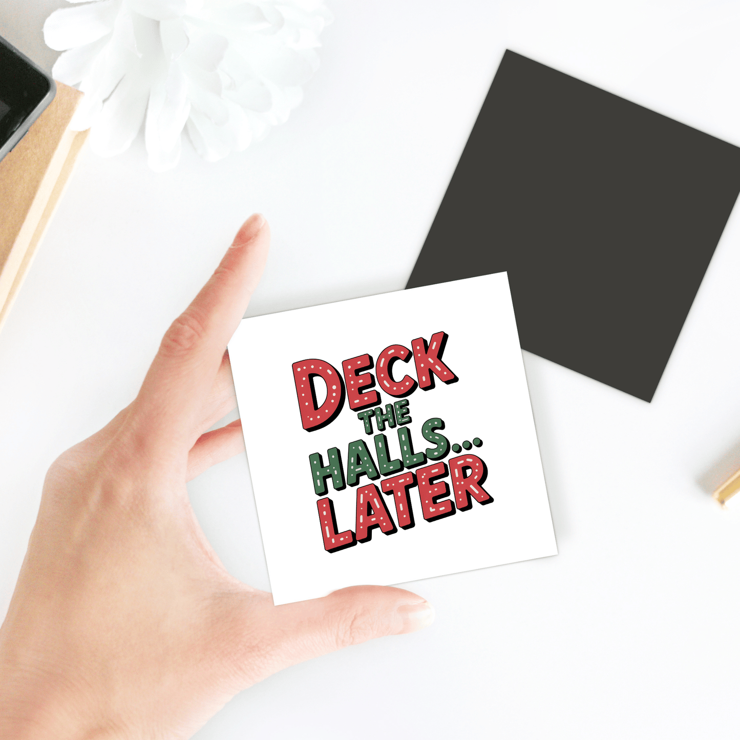 A hand holds the "Deck The Halls... Later Magnet" by Mirabilia Boutique, featuring festive red and green text. This funny Christmas gift is a perfect holiday or fridge magnet and makes a great stocking stuffer for humor lovers.