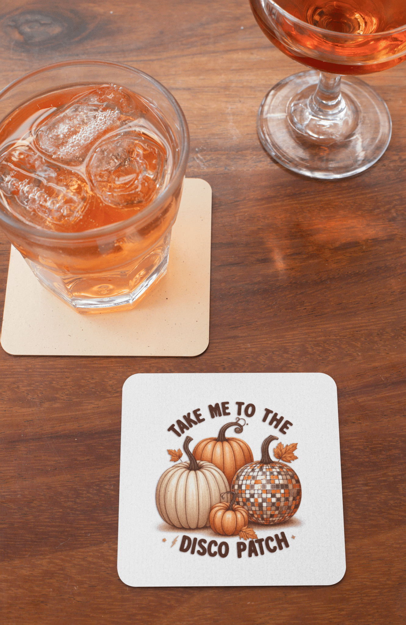 Two drinks sit on Mirabilia Boutique's Disco Patch Pumpkin Coaster Set, featuring retro pumpkins and a silver disco ball with "Take me to the disco patch"—fun fall decor for parties and entertaining.