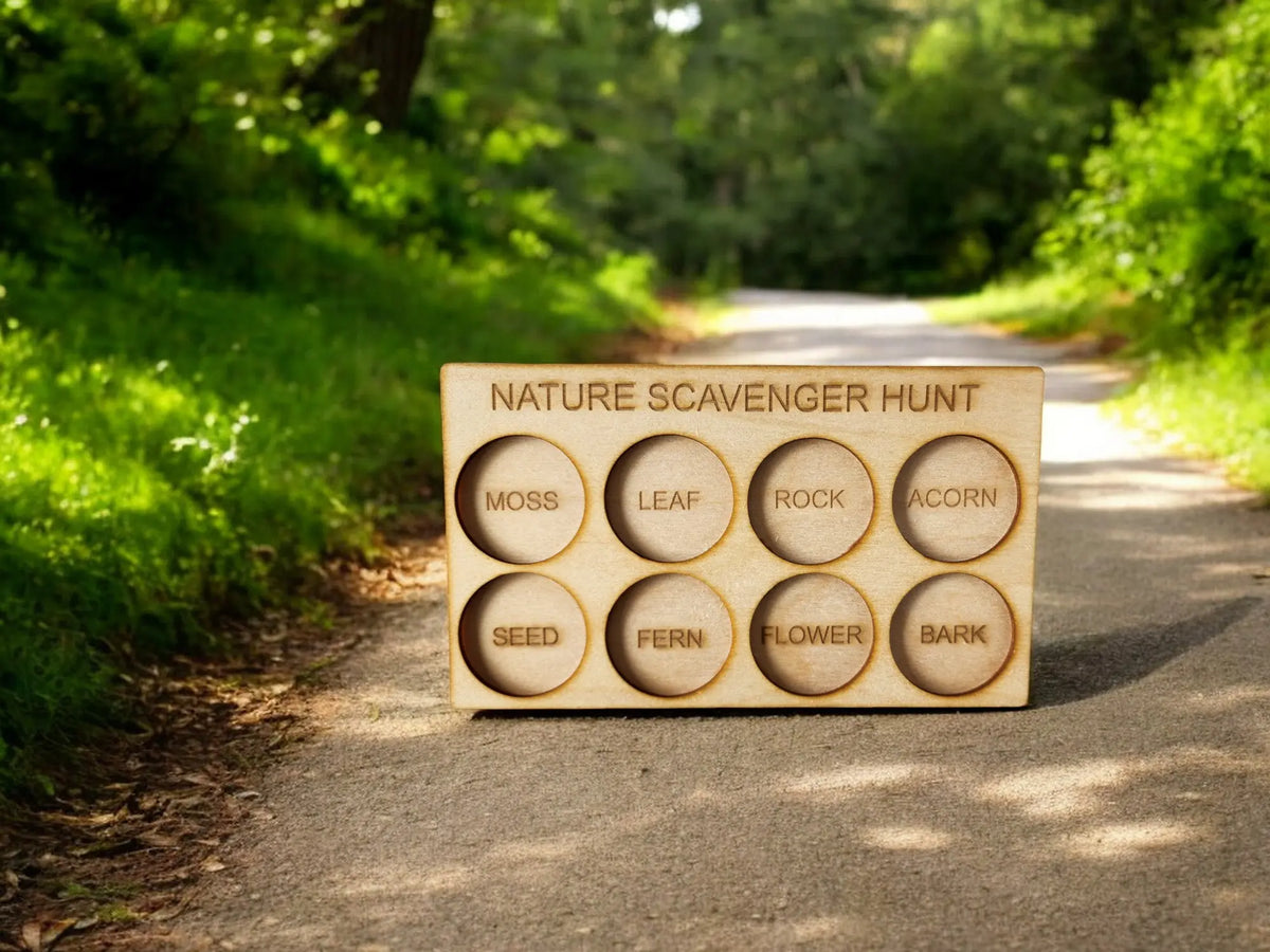 The "Nature Scavenger Hunt for Kids: Fun Outdoor Adventure Game" by Mirabilia Boutique features an eco-friendly wooden board displaying cutouts labeled with nature items such as moss, leaf, rock, acorn, seed, fern, flower, and bark. This engaging outdoor toy is nestled on a pathway surrounded by lush greenery.