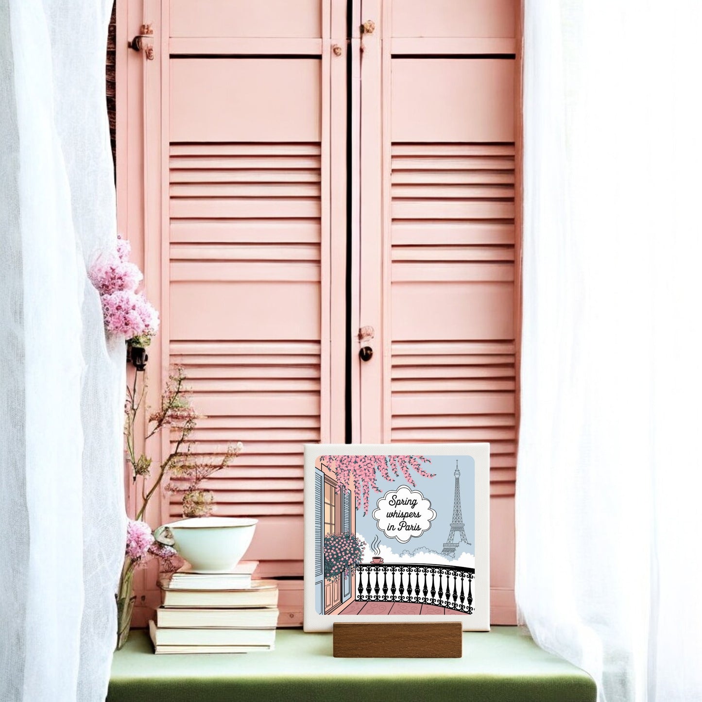 The "Spring Whispers in Paris Mini Sign - Soft Paris Spring" by Mirabilia Boutique features an Eiffel Tower design on a handcrafted wood block, beautifully displayed among books, flowers, and a teacup—ideal for your spring decor.