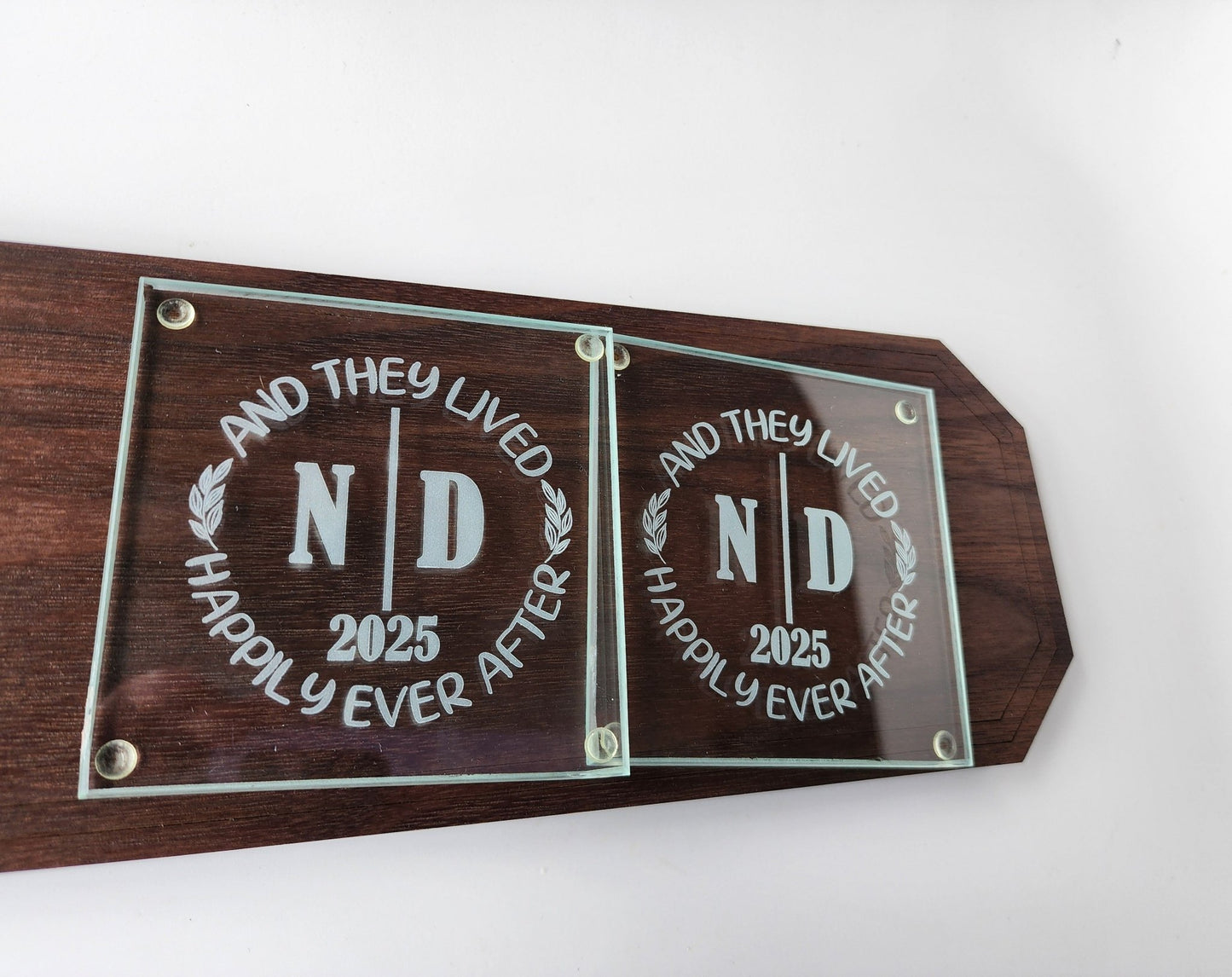 The Personalized Glass Wedding Coasters from Mirabilia Boutique feature custom engravings like "AND THEY LIVED HAPPILY EVER AFTER" encircling "N D 2025." A perfect romantic home décor gift for any wedding couple.