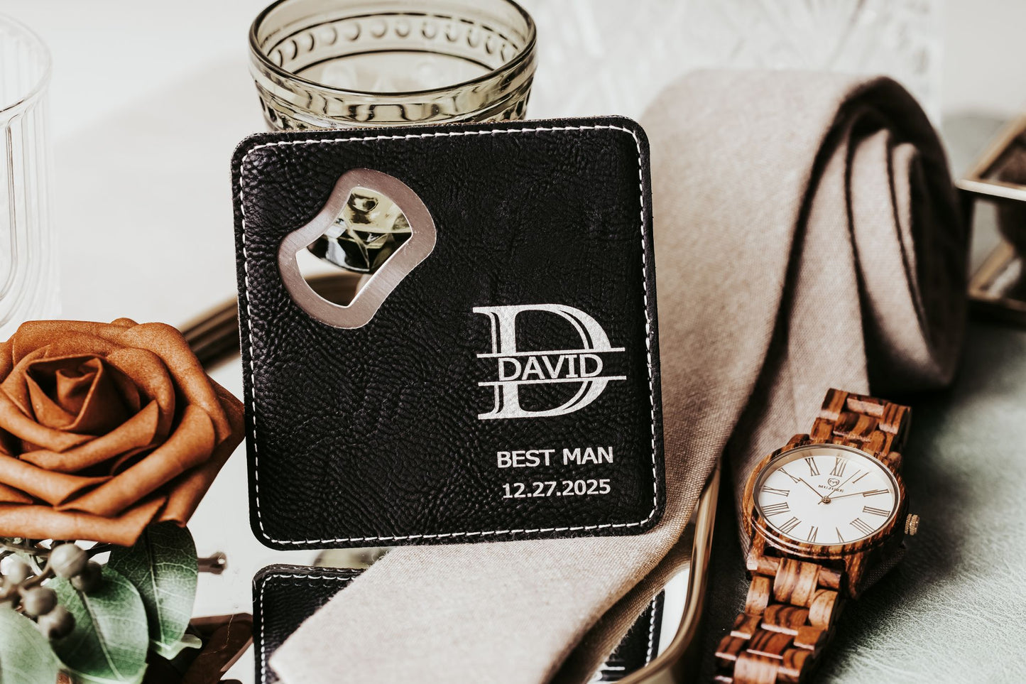 A unique groomsman gift from Mirabilia Boutique, this engraved leatherette bottle opener coaster features "DAVID," "BEST MAN," and "12.27.2025" surrounded by a brown rose, beige tie, glass, and wooden wristwatch design.
