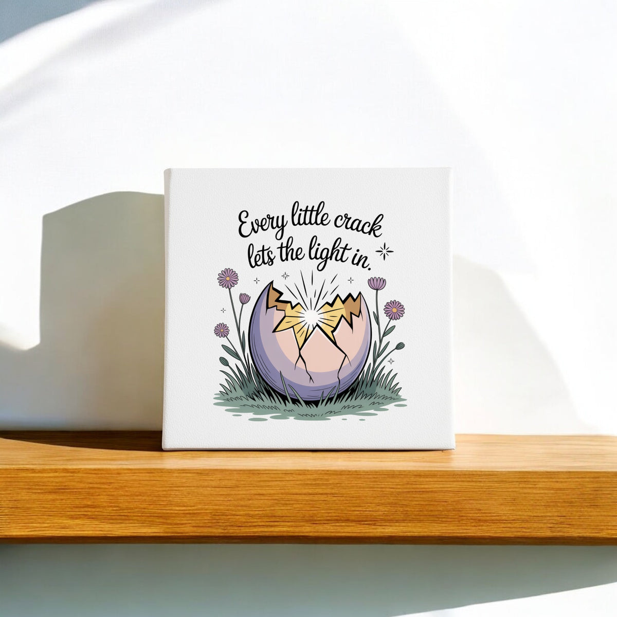 The Every Little Crack Lets the Light In Canvas Art by Mirabilia Boutique features a cracked egg with light shining through and flowers, plus the uplifting quote, making it perfect inspirational wall decor.
