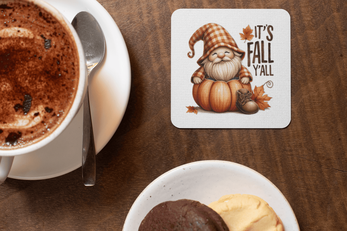 A cup of hot chocolate and cookies rest beside a Mirabilia Boutique Fall Gnome Coaster featuring "It's Fall Y'all"—the perfect cozy autumn decor for your wooden table.