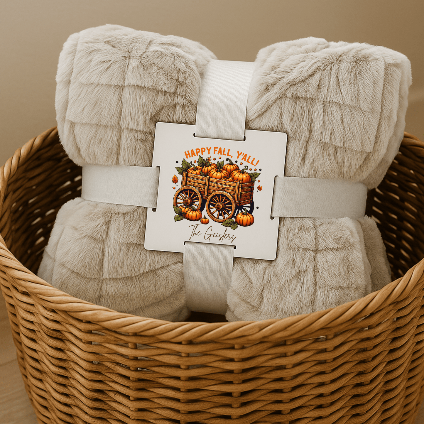 The Mirabilia Boutique Custom Fall Throw Blanket is a cozy beige autumn gift, rolled in a wicker basket with ribbon and card—“Happy Fall, Y’all! The Gardners”—featuring a pumpkin wagon. A unique seasonal touch for any home.