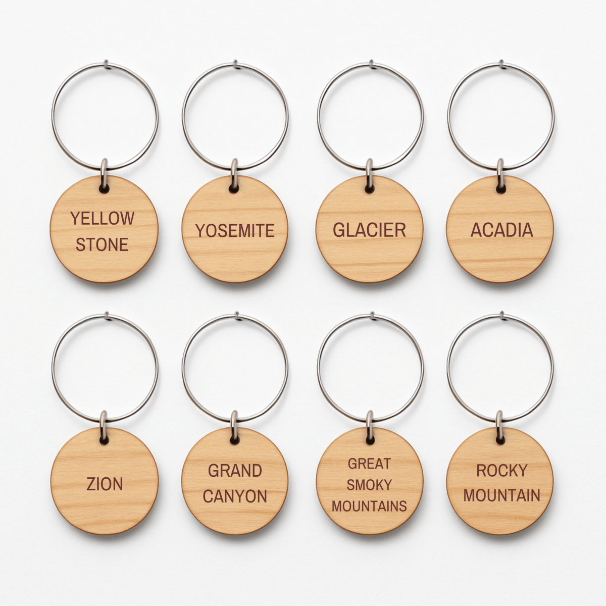 Set of eight round wooden keychains with metal rings by Mirabilia Boutique, each engraved with a national park—ideal for your parks collection or as unique "Favorite National Parks Wine Charms.