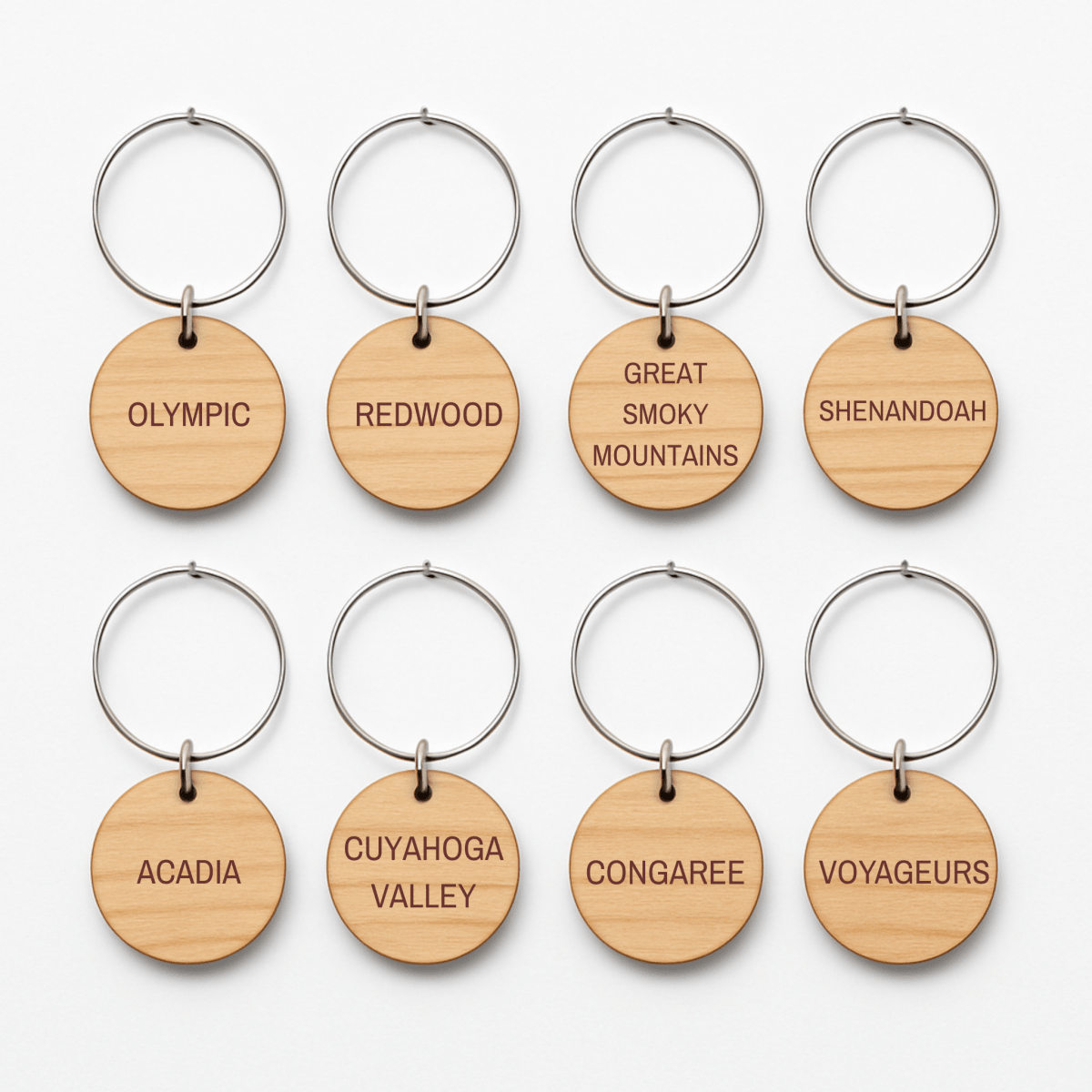 Eight Forest And Fog Wine Charms by Mirabilia Boutique are arranged in two rows, each featuring a U.S. national park’s name—perfect for nature lovers who admire woodland landscapes like Olympic, Redwood, Shenandoah, and more.