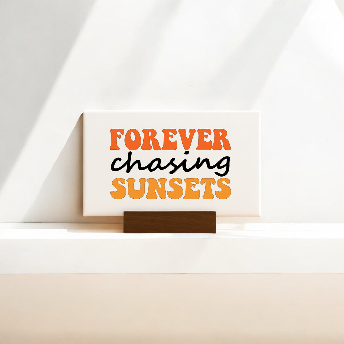 The Mirabilia Boutique "Forever Chasing Sunsets Canvas – Retro Mini Sign" features bold orange and black text on a bright background with sunlit shadows—a charming decor piece for sunset lovers and mini canvas art fans.