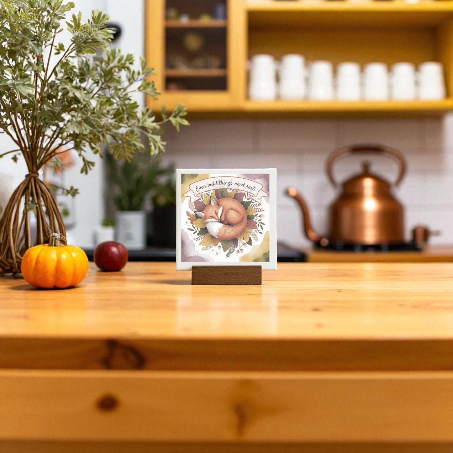 A wooden kitchen table with a small pumpkin, apple, potted plant, and mushroom card brings woodland charm. In the background, shelves with yellow mugs and the Fox Nature Art Print by Mirabilia Boutique add warmth to the white subway tile backsplash.