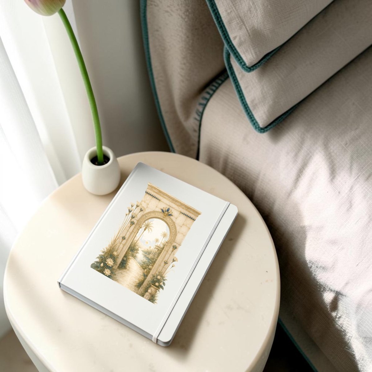 The Garden Path Journal | Ancient Egyptian Inspired Notebook from Mirabilia Boutique, adorned with an archway and garden illustration from the Lapis & Lotus Collection, rests on a round bedside table beside a bed and a white vase holding a single tulip.