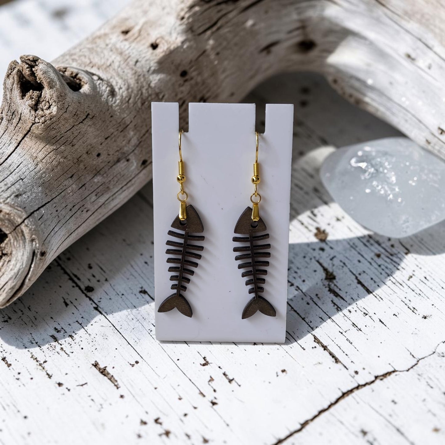Fishbone Earrings | Lasercut Walnut Wood by Mirabilia Boutique feature gold hooks and are displayed on a white card atop rustic wood—ideal for adding coastal vibes to your style.