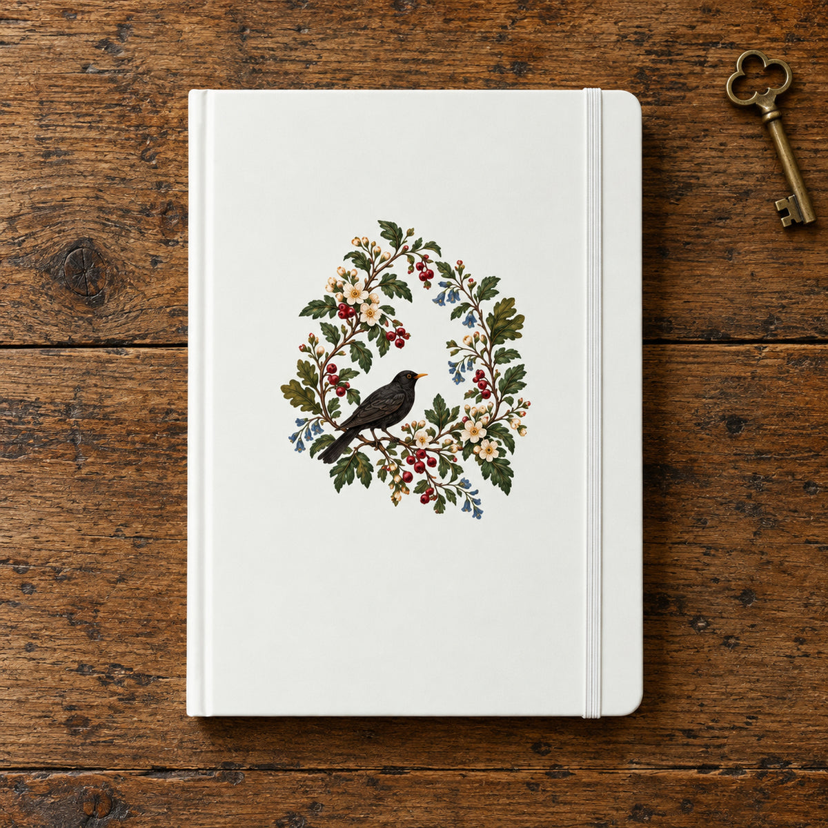 The Garden Ledger A5 Lined Journal by Mirabilia Boutique, featuring a central botanical wreath illustration of a blackbird among leaves, flowers, and berries, resting on a wooden surface next to an antique key.