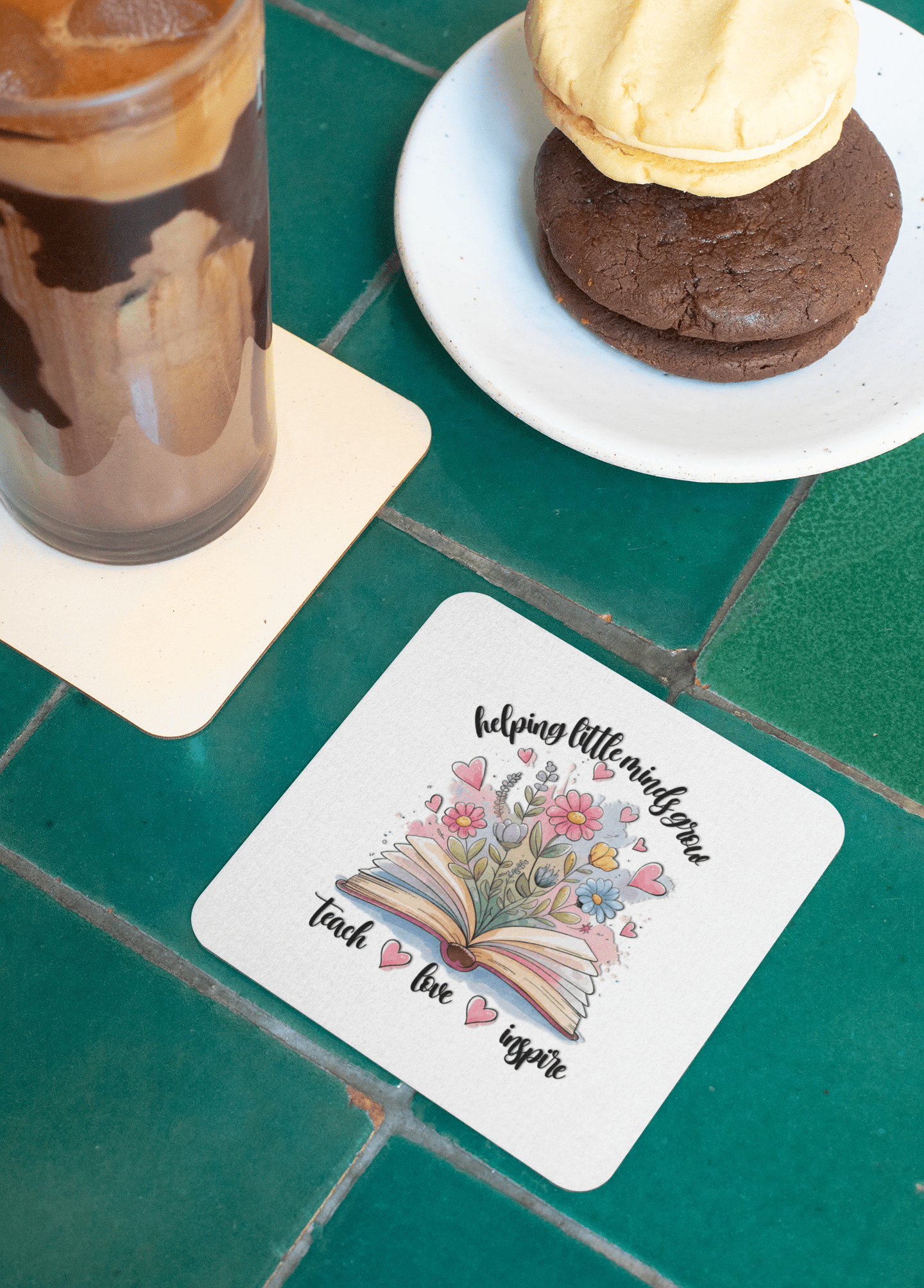 A close-up of the Helping Little Minds Grow Coasters teacher gift set by Mirabilia Boutique rests on a green tiled table with a drink and cookies—an ideal gift for inspiring teachers.