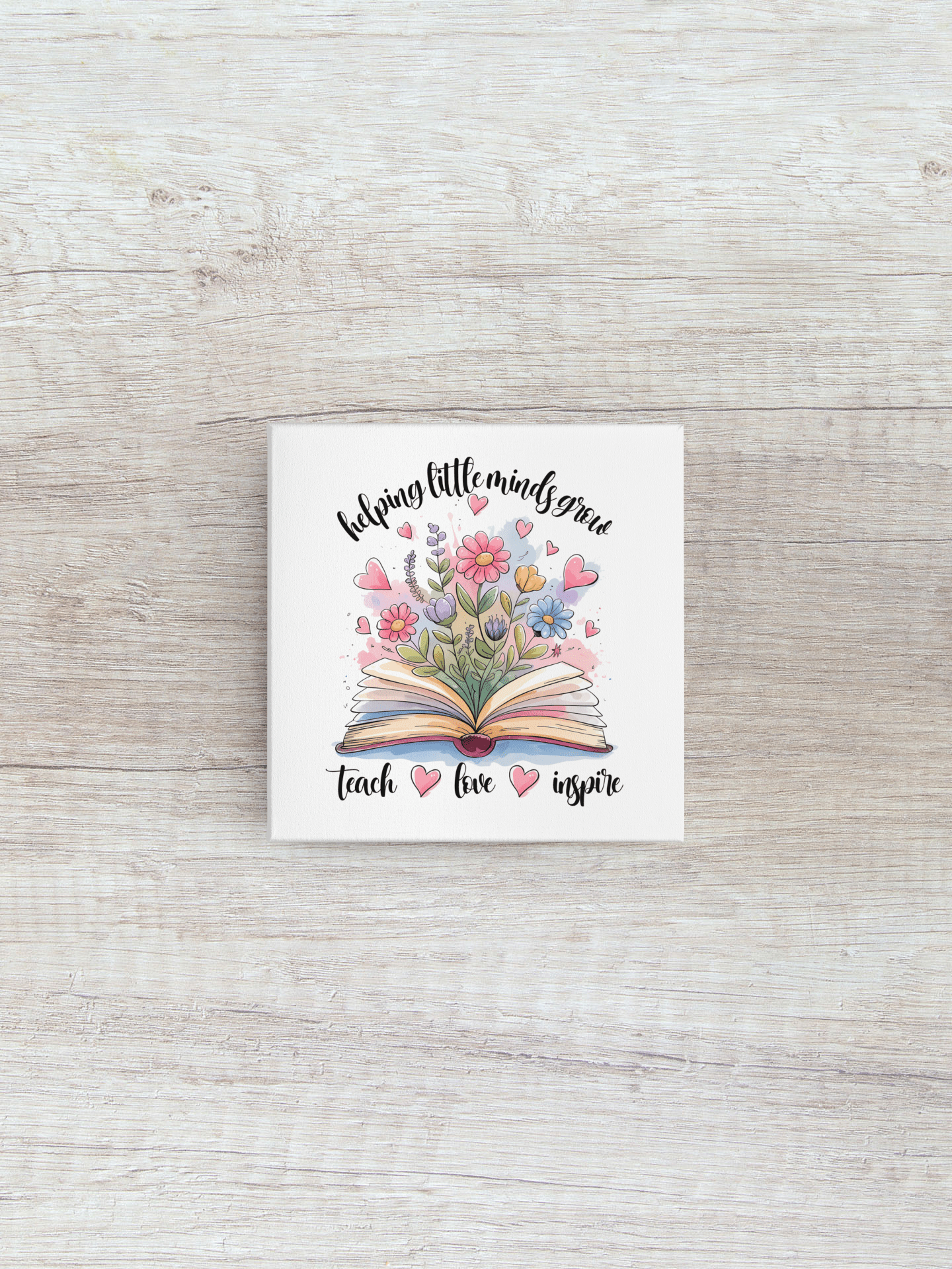 The Helping Little Minds Grow Mini Canvas by Mirabilia Boutique features colorful flowers blooming from a book with inspiring words—an ideal teacher gift or classroom decor. Includes easel for display.