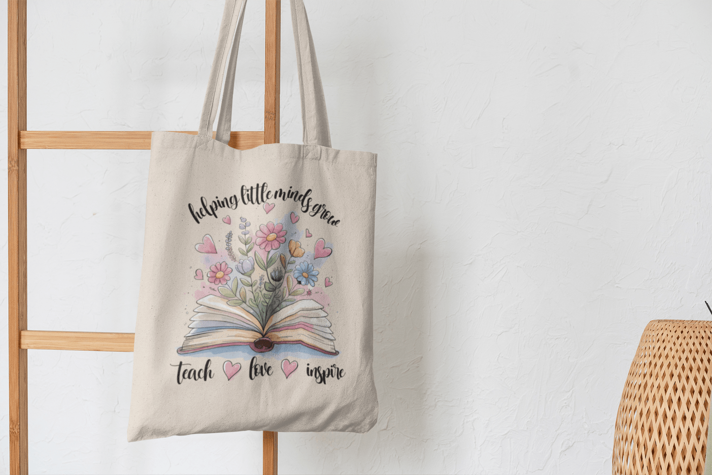 The Helping Little Minds Grow Tote Bag by Mirabilia Boutique is a beige canvas teacher bag with a book and floral design, plus the phrase "helping little minds grow, teach, love, inspire"—a perfect teacher appreciation gift.