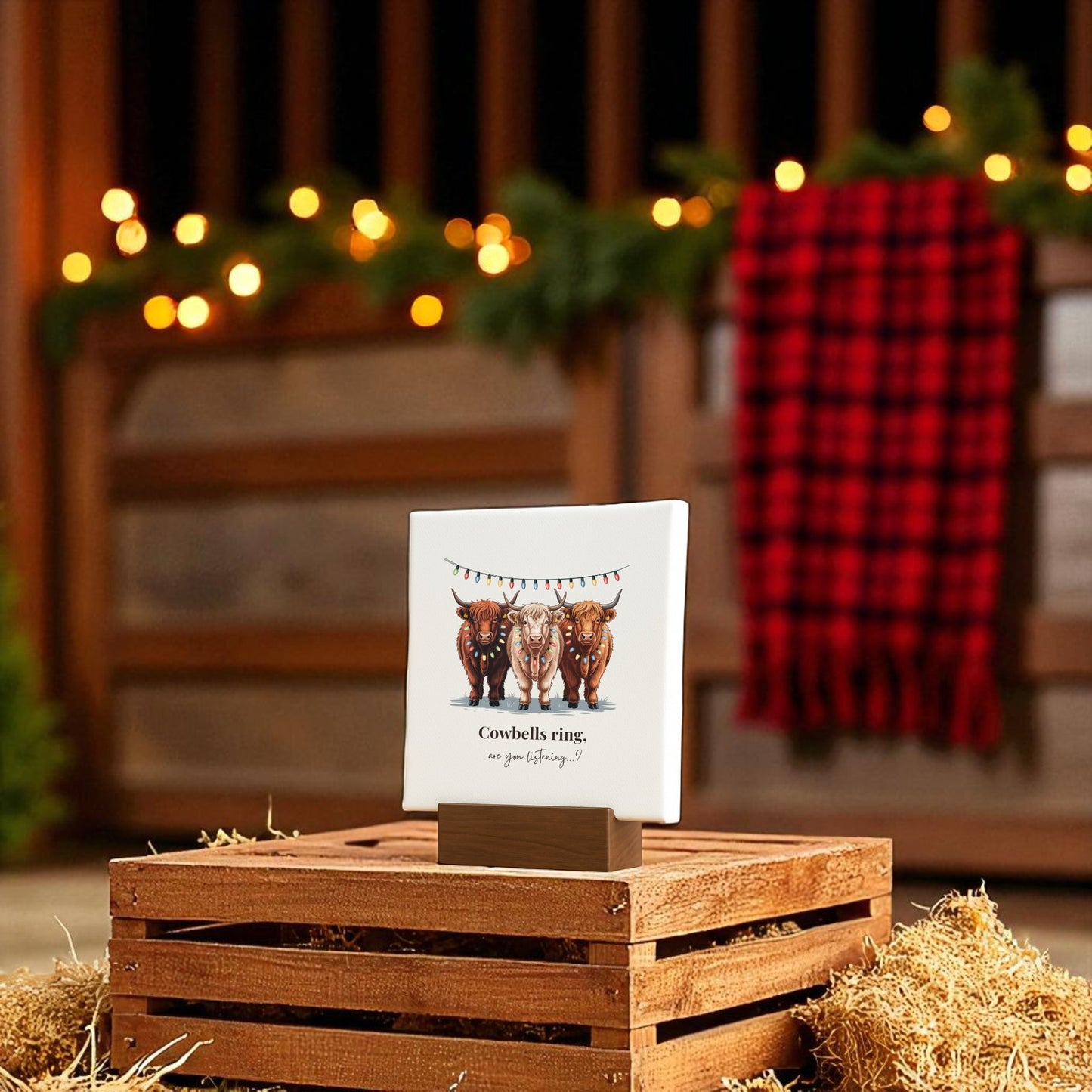 The Highland Cow Christmas Mini Sign by Mirabilia Boutique features cows and festive lights with "Cowbells ring, are you listening?" on a 4x4 rustic decor piece, perfect for farmhouse holiday charm amid glowing lights and greenery.