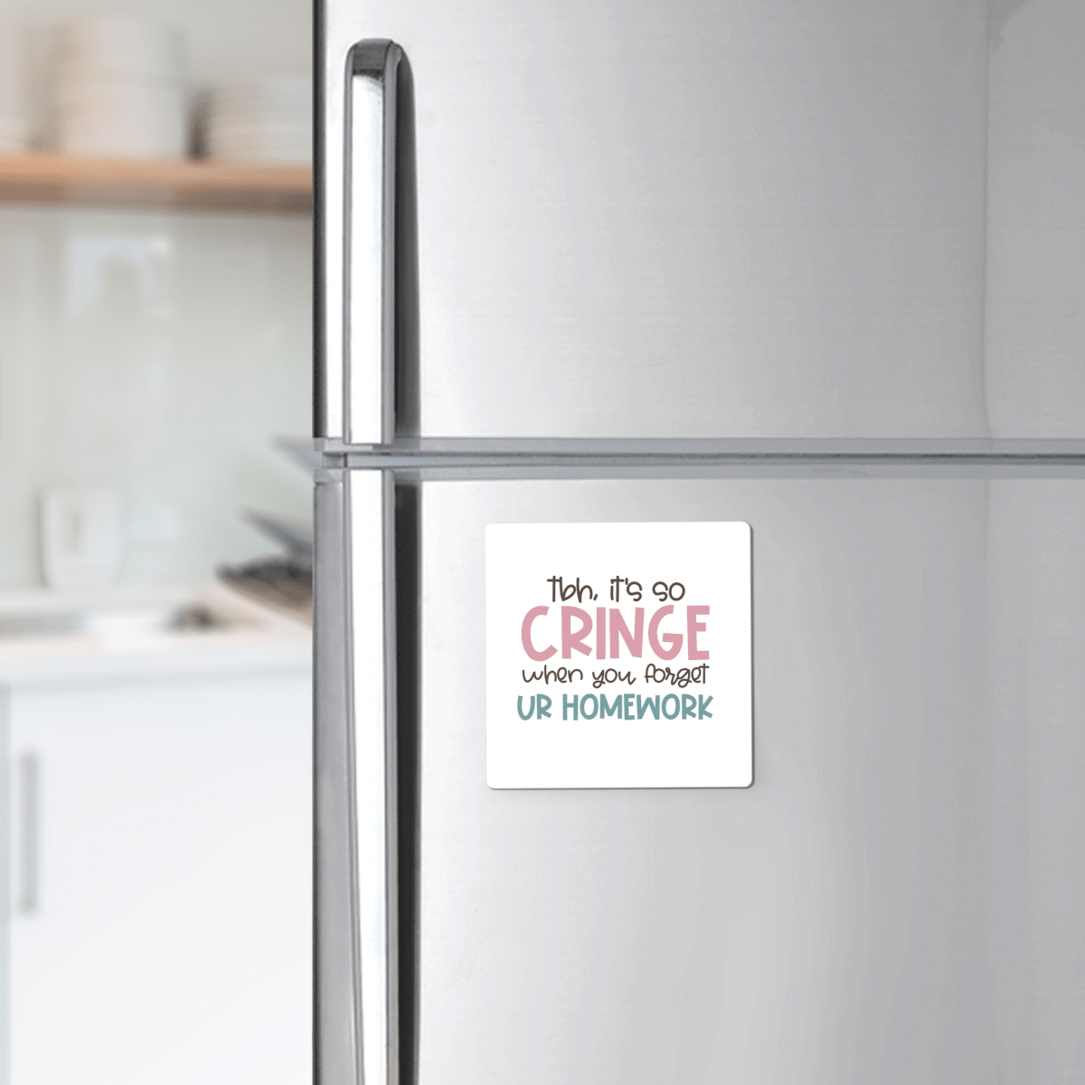 The "It's So Cringe Forget Your Homework Magnet" by Mirabilia Boutique is a square white magnet with playful text, perfect for your fridge. Makes a fun teacher gift or classroom decor—kitchen shelves with dishes in the background.